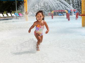 a girl playing next to fountains that are splashing water