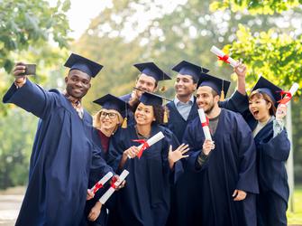 A group of students wearing graduation gowns and caps take a photo together while holding their diplomas.
