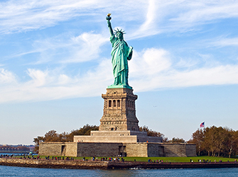 A large, green copper statue of a woman holding a torch, standing on a pedestal.