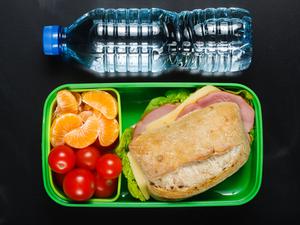A photo of a school lunch. There is a bottle of water and a container with oranges, tomatoes, and a sandwich.