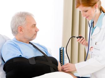A doctor taking the blood pressure of a man with his arm in a sling.