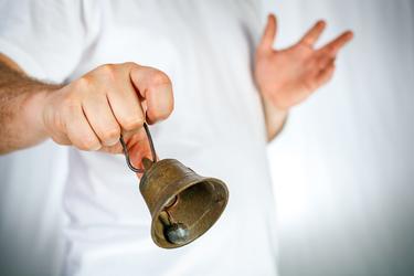 A person in a white shirt is holding a small metal bell out in the air.