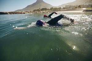 two people with wetsuits and swim caps on swimming in an open body of water